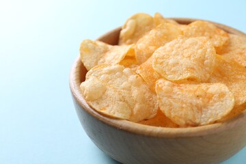 Tasty potato chips in bowl on light blue background, closeup. Space for text