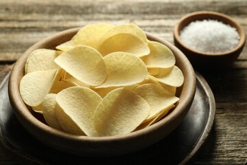 Tasty chips and salt on wooden table, closeup