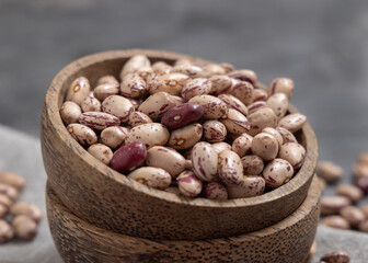 Wooden bowl full of dried raw pinto beans on gray closeup. Traditional Latin American legumes
