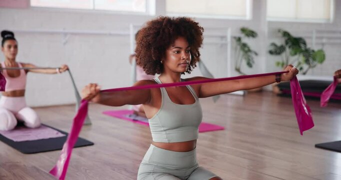 Fitness class, pilates and resistance band with people in studio for exercise or training together. Equipment, stretching and tension with instrcutor in group session at gym for strength workout