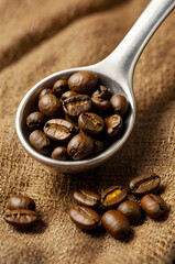Obraz premium Roasted Coffee Beans in a Spoon: A close-up shot captures the rich, dark brown roasted coffee beans nestled in a metallic spoon, set against a textured burlap background.