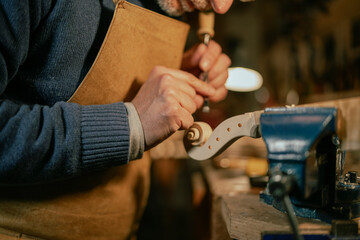 Luthier carefully carving violin scroll with gouge in workshop
