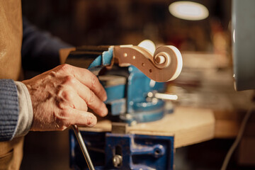 Luthier crafting violin scroll in workshop using vise