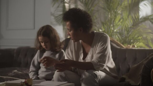 Black woman sitting on sofa teaching daughter solfeggio music