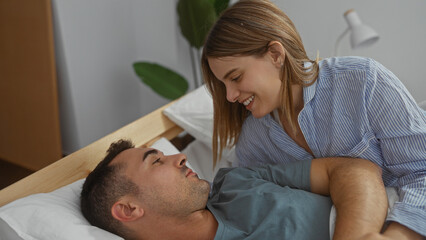 Woman smiling at man lying in bed in cozy bedroom setting under soft indoor lighting showing a warm intimate moment between the couple emphasizing love and tranquility.