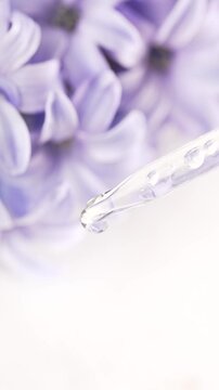 Serum drop falling from pipette on flowers background. Cosmetic or medical liquid in slow motion. Natural and organic skin or body care products