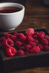 Fresh raspberries and cup of tea on wooden table