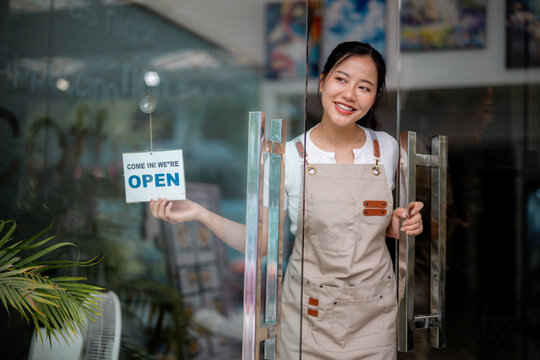 Female shopkeeper opening glass door, flipping storefront sign, welcoming morning customers
