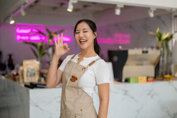 Young asian barista gesturing ok sign while working behind cafe counter