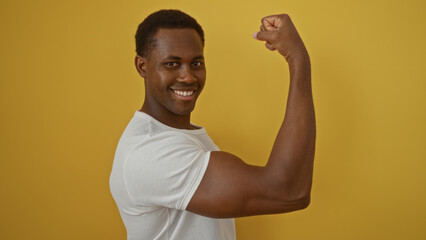 Young african american man smiling confidently flexing arm isolated against bright yellow background