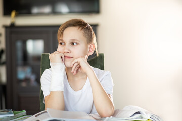 Kid teenager boy pupil at home making homework with broken finger. Child hand with a cast.
