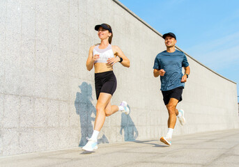 Two runners jog along a modern urban pathway on a sunny day