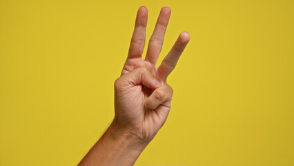 Naklejka premium Man holding up three fingers against a bright yellow background