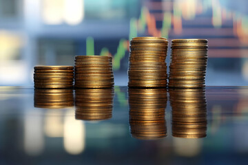 Stacked gold coins reflecting in a table with a financial stock market graph displayed in the background, representing investment success.