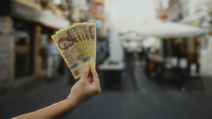 Hand holding hungarian forint banknotes on a bustling city street background, featuring an outdoor...