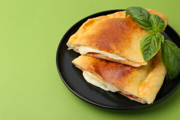 Pieces of delicious calzone pizza with mozzarella, tomatoes and basil on green background, closeup