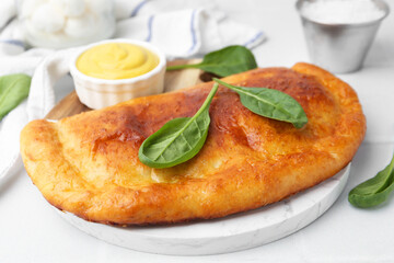 Tasty calzone with basil and sauce on white table, closeup