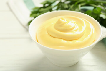 Delicious mayonnaise sauce in bowl and parsley on white wooden table, closeup