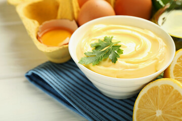 Delicious mayonnaise sauce with parsley in bowl and ingredients on white wooden table, closeup