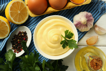 Delicious mayonnaise sauce with parsley in bowl and ingredients on white wooden table, flat lay