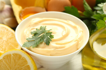 Delicious mayonnaise sauce with parsley in bowl and ingredients on table, closeup