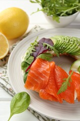 Delicious bagel with salmon, cream cheese, cucumber and avocado on white wooden table, closeup
