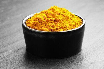Turmeric powder in bowl on grey table, closeup