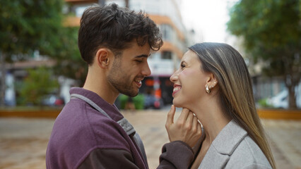 Man and woman smiling at each other in love at an urban park, capturing the essence of a beautiful couple in a city outdoor setting, conveying a strong relationship and connection.