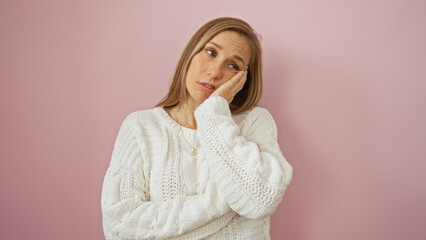 Woman with hand on cheek looking thoughtful against a pink wall wearing a cozy sweater, isolated in...