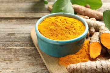 Turmeric powder in bowl, roots and leaves on wooden table, closeup. Space for text