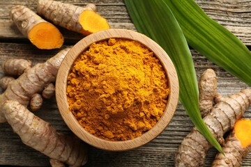 Turmeric powder in bowl, roots and leaves on wooden table, flat lay