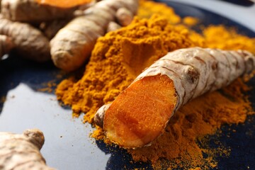 Aromatic turmeric powder and fresh roots on blue plate, closeup