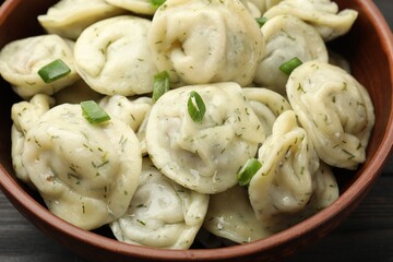 Tasty dumplings with green onion and dill in bowl on wooden table, above view