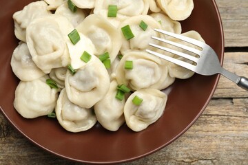 Tasty dumplings with green onion and fork on wooden table, top view