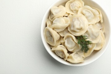 Tasty dumplings and dill in bowl on white table, top view. Space for text