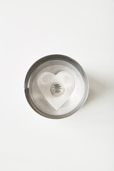 Heart shaped cookie cutter with a silver exterior and white interior placed on a plain background