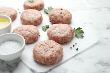Many uncooked patties and spices on white marble table, closeup