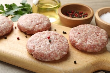 Many uncooked patties and spices on wooden table, closeup