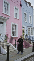 Woman standing in chelsea street with colorful houses in london wearing a coat capturing a vibrant urban scene.