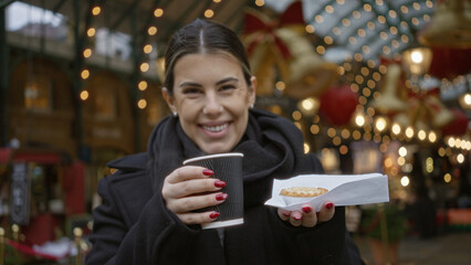 Woman smiling in covent garden holding coffee and snack with festive christmas lights in london street showcasing joyful hispanic holiday scene.