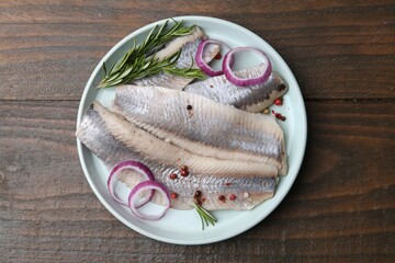 Marinated herring fillets with onion rings, rosemary and peppercorns on wooden table, top view