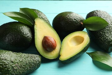 Whole and cut avocados on light blue wooden table, closeup