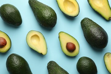 Whole and cut avocados on light blue background, flat lay