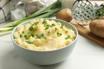 Delicious mashed potato with green onions in bowl on white marble table, closeup