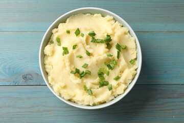Delicious mashed potato with green onions in bowl on light blue wooden table, top view