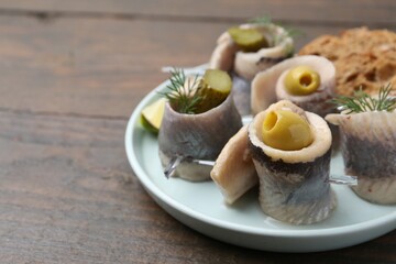 Delicious herring rolls with olives, pickles and dill on wooden table, closeup. Space for text