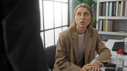 Woman sitting at desk in office looks up listening during business meeting, emphasizing indoor...