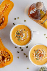 Roasted butternut squash soup with cream and pumpkin seeds on two white mugs.
