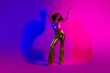 Trendy young woman dancing in neon-lit studio, showcasing vibrant fashion and glowing style