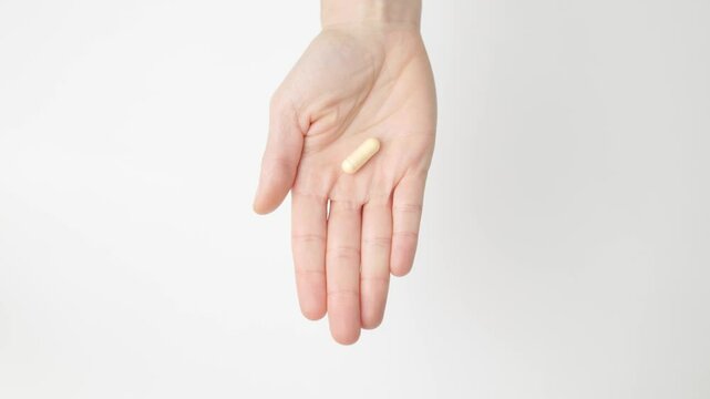 A woman's hand opens showing a q10 coenzyme capsule pill, on her palm, on white background, copy space